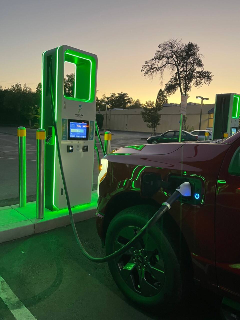 A red Ford F-150 Lightning is plugged into a charger at night. The charger glows green. 